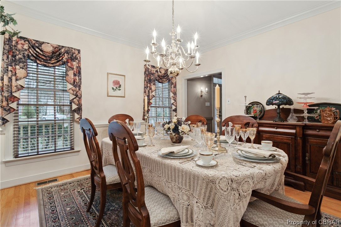 Dining space with a chandelier, wood-type flooring, and ornamental molding
