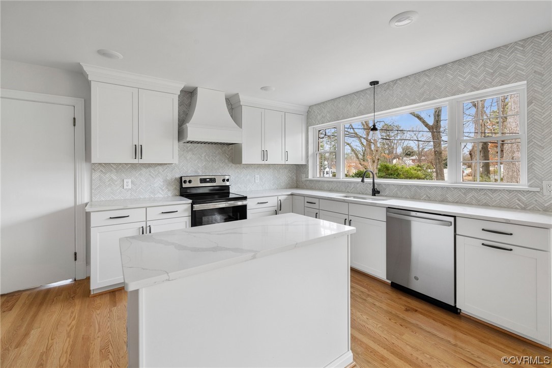Kitchen with white cabinetry, light hardwood / wood-style flooring, appliances with stainless steel finishes, and custom range hood