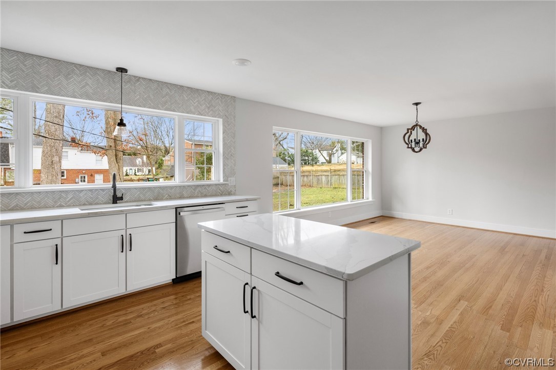 Kitchen with stainless steel dishwasher, light hardwood / wood-style flooring, tasteful backsplash, and white cabinets