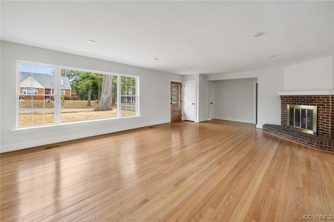 Unfurnished living room featuring light hardwood / wood-style flooring and a brick fireplace