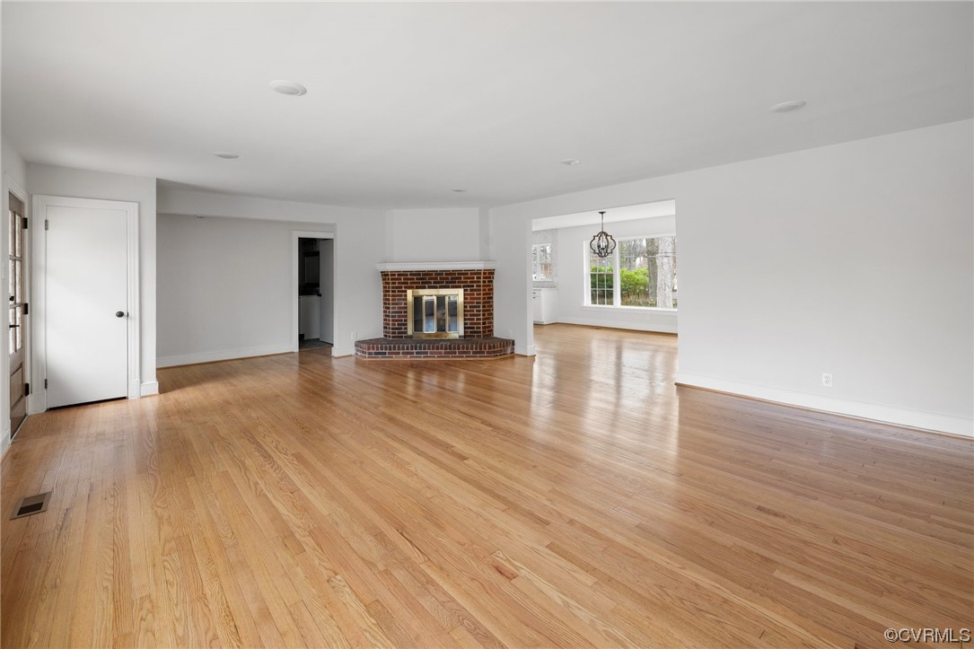Unfurnished living room with light wood-type flooring, a notable chandelier, and a brick fireplace