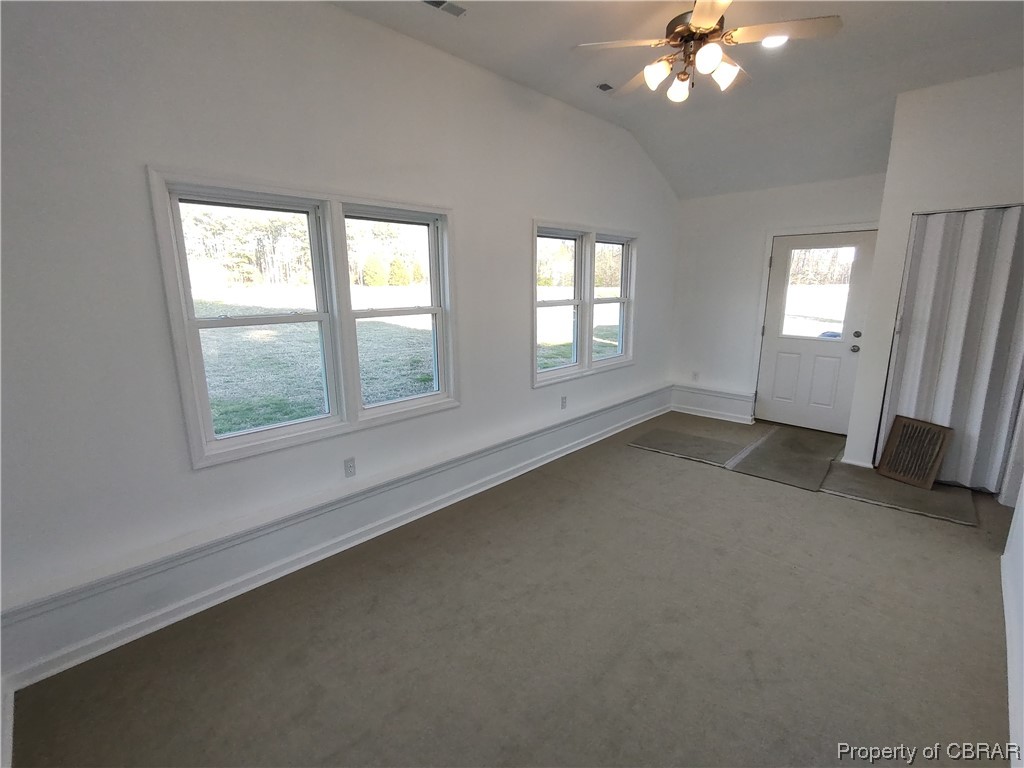 Spare room with lofted ceiling, ceiling fan, and dark carpet