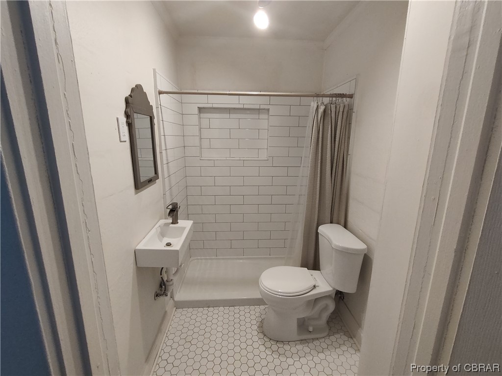 Bathroom with toilet, sink, tile floors, and curtained shower