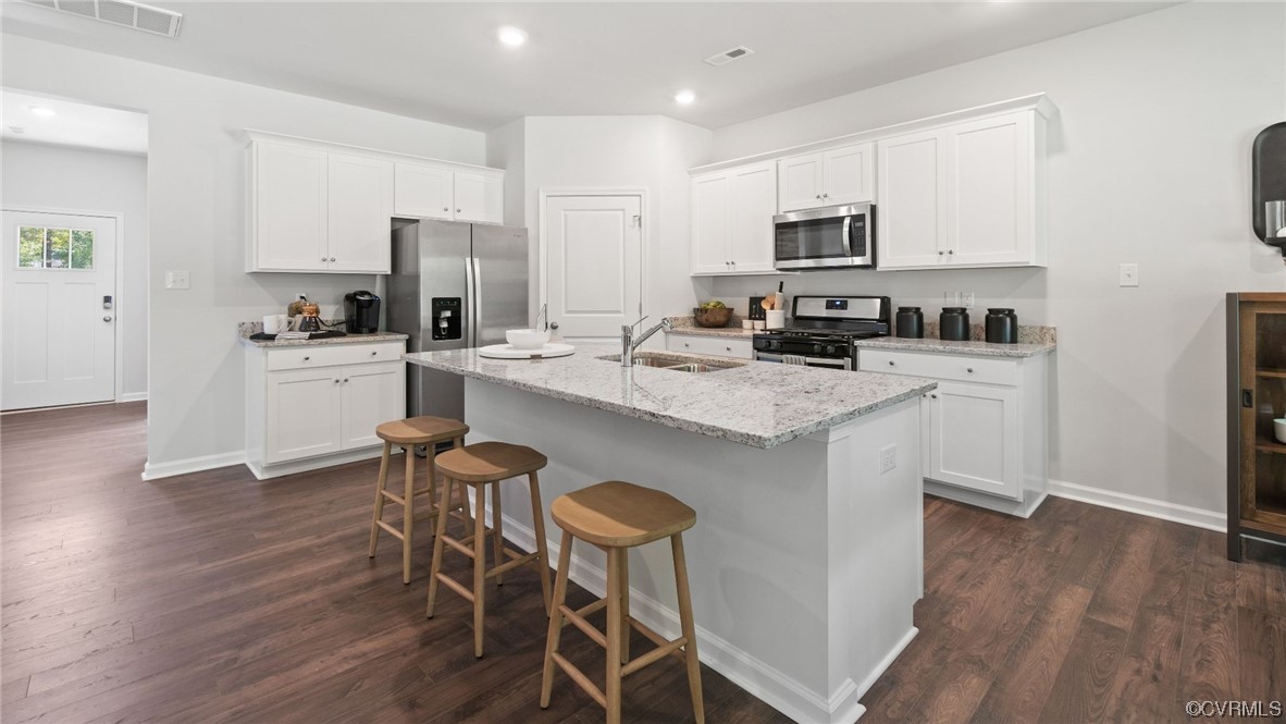 Kitchen with white cabinets, appliances with stainless steel finishes, a center island with sink, and dark wood-type flooring