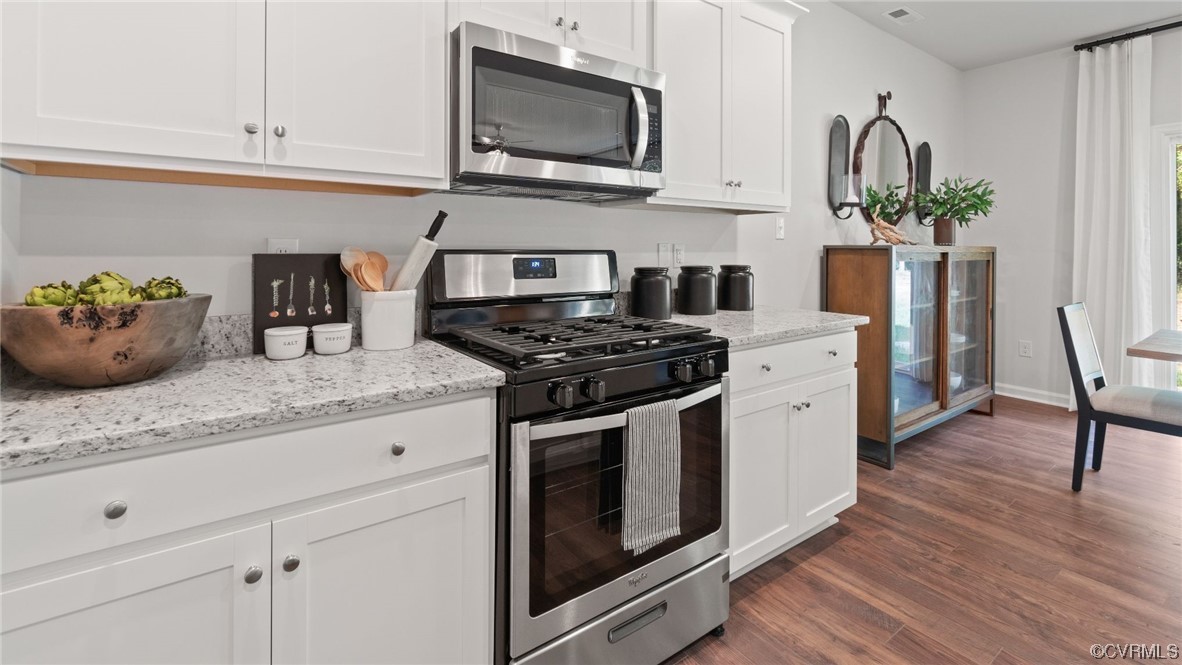 Kitchen featuring light stone countertops, dark hardwood / wood-style flooring, stainless steel appliances, and white cabinets