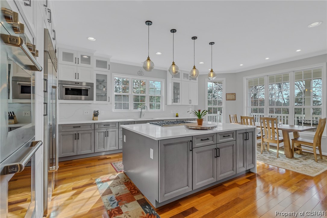 Kitchen with light wood-type flooring, pendant lighting, a kitchen island, sink, and gray cabinetry