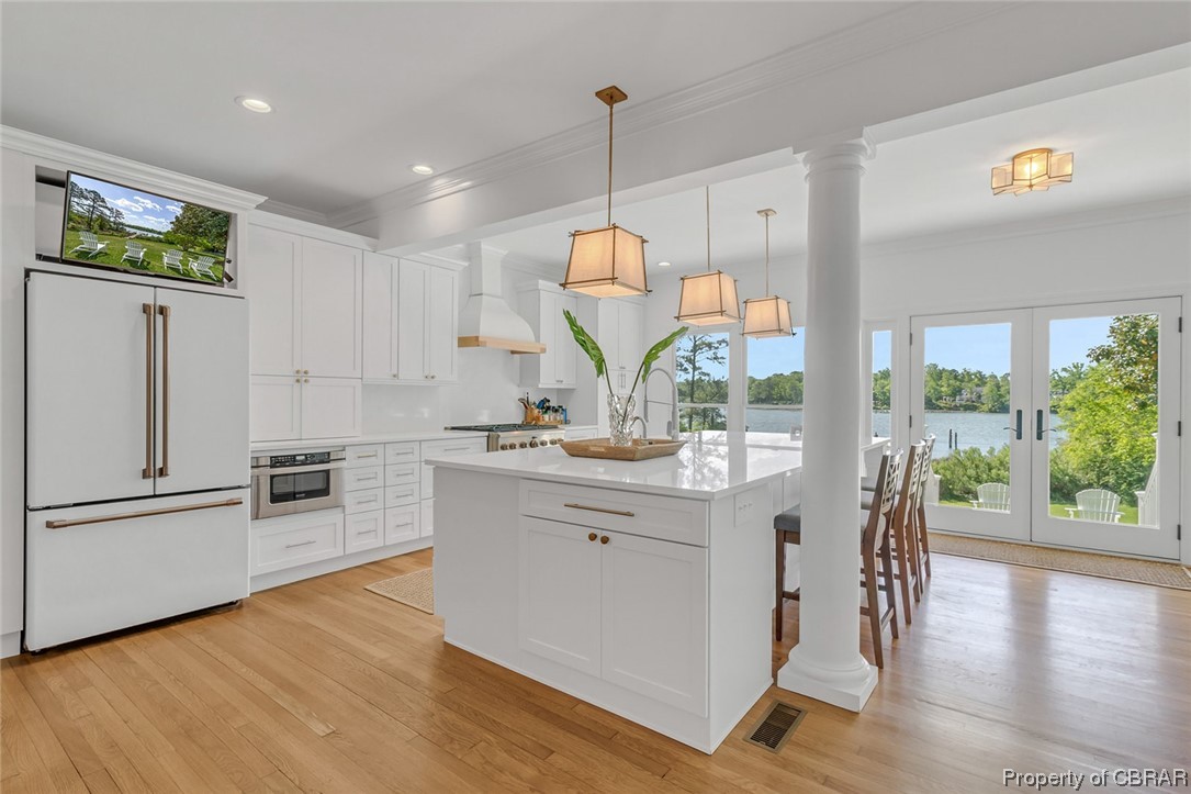Kitchen featuring white cabinets, hanging light fixtures, appliances with stainless steel finishes, and a kitchen island with sink