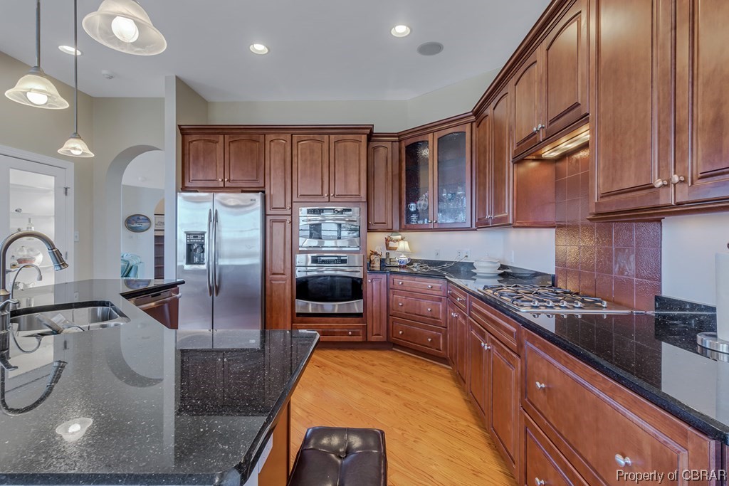 Kitchen featuring light hardwood / wood-style floors, backsplash, hanging light fixtures, sink, and stainless steel appliances