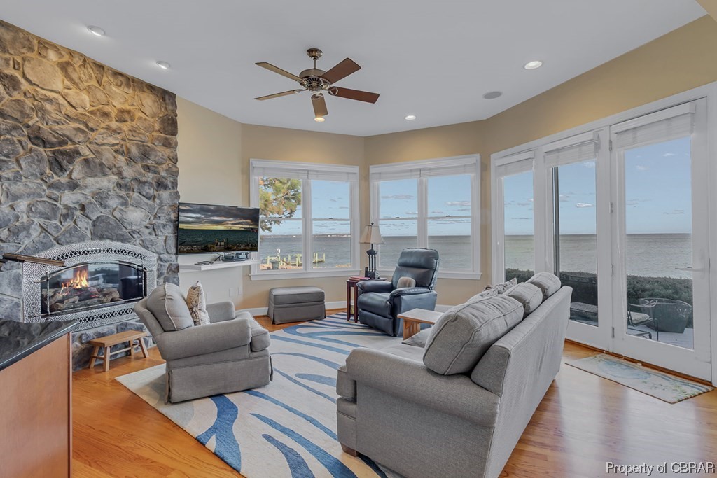 Living room with light hardwood / wood-style floors, a water view, ceiling fan, and a stone fireplace