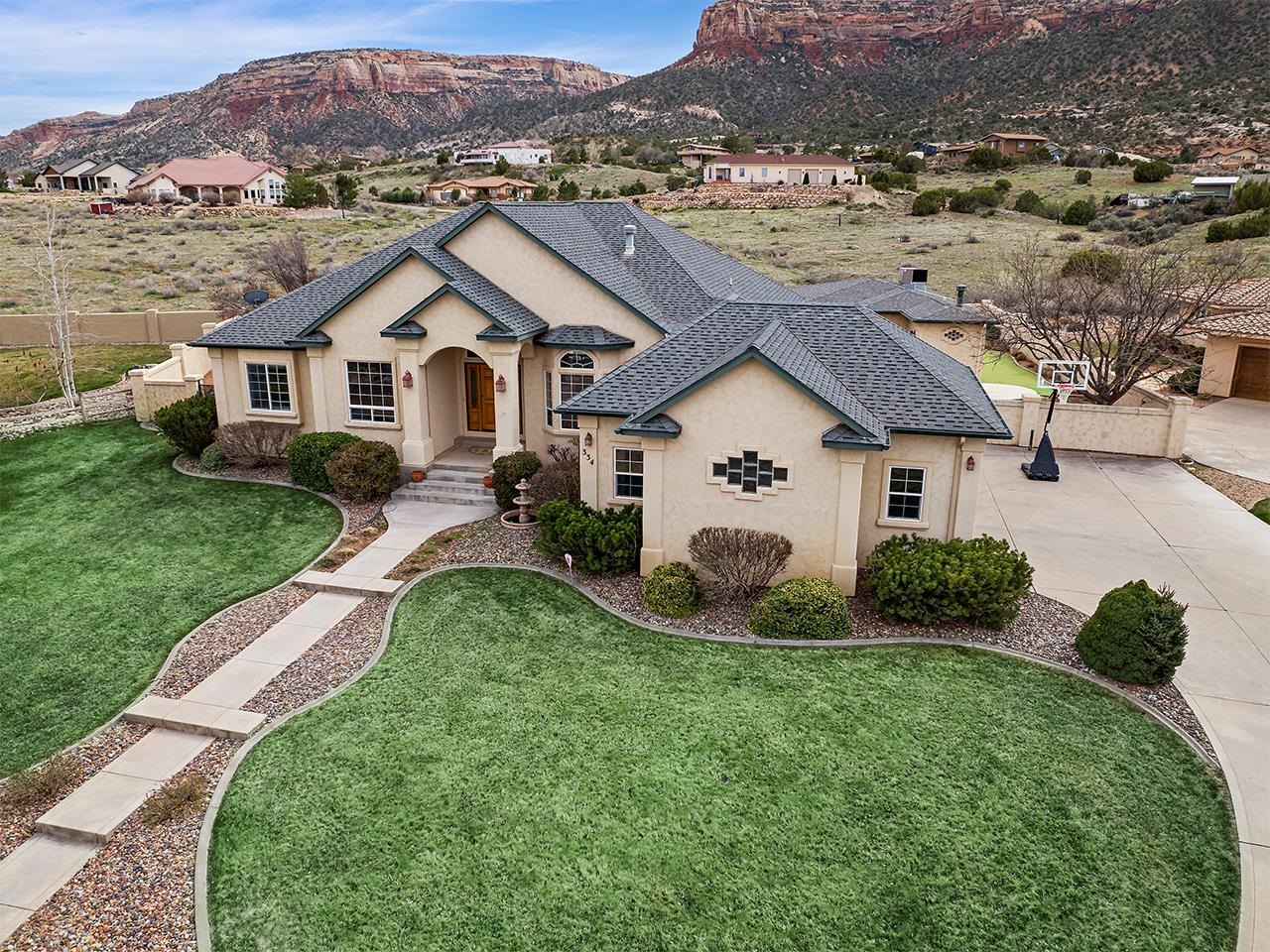 Welcome to your dream home! This luxurious property offers an exceptional lifestyle with incredible views and resort-style amenities. Boasting over 4,000 sq. ft of living space, this home features a pool, hot tub, and a guesthouse/pool house that is perfect for hosting guests. As you step inside the beautiful entry, you are greeted by an elegant dining room and custom wood flooring. The main living area is spacious and open, offering plenty of room for entertaining. The living room features large windows that offer stunning views of the Colorado National Monument and surrounding landscape, with larger acreage properties to the south. The wonderful updated kitchen is built for entertaining, with bar seating, a large eat-in kitchen area and access to the patio. The primary suite is a private retreat, featuring a large bedroom with beautiful views and an area for relaxing, plus an updated bathroom, and a roomy walk-in closet. Additional bedrooms and bathrooms are spacious and well-appointed. For those who work from home, this property also features a private office that offers a quiet space for concentration and productivity. The basement level offers a home theater and game room with wet bar and an additional bedroom and bathroom. The outdoor living spaces are just as impressive as the interior, with a sparkling pool that is perfect for fun in the sun.  The hot tub provides a relaxing oasis with incredible views for soaking after a long day or take a steam shower in the pool house. The covered patio and outdoor kitchen are ideal for al fresco dining and entertaining guests. There are also raised garden beds, a fire pit, and a putting green within the private, secure, walled backyard filled with mature landscaping. The oversized two-car garage and generous driveway give you room for vehicles and storage. This property is situated in a desirable neighborhood on a cul-de-sac, and is close to schools, trails, and shopping.  Don't miss your chance to own this stunning home and enjoy the luxurious lifestyle it has to offer!