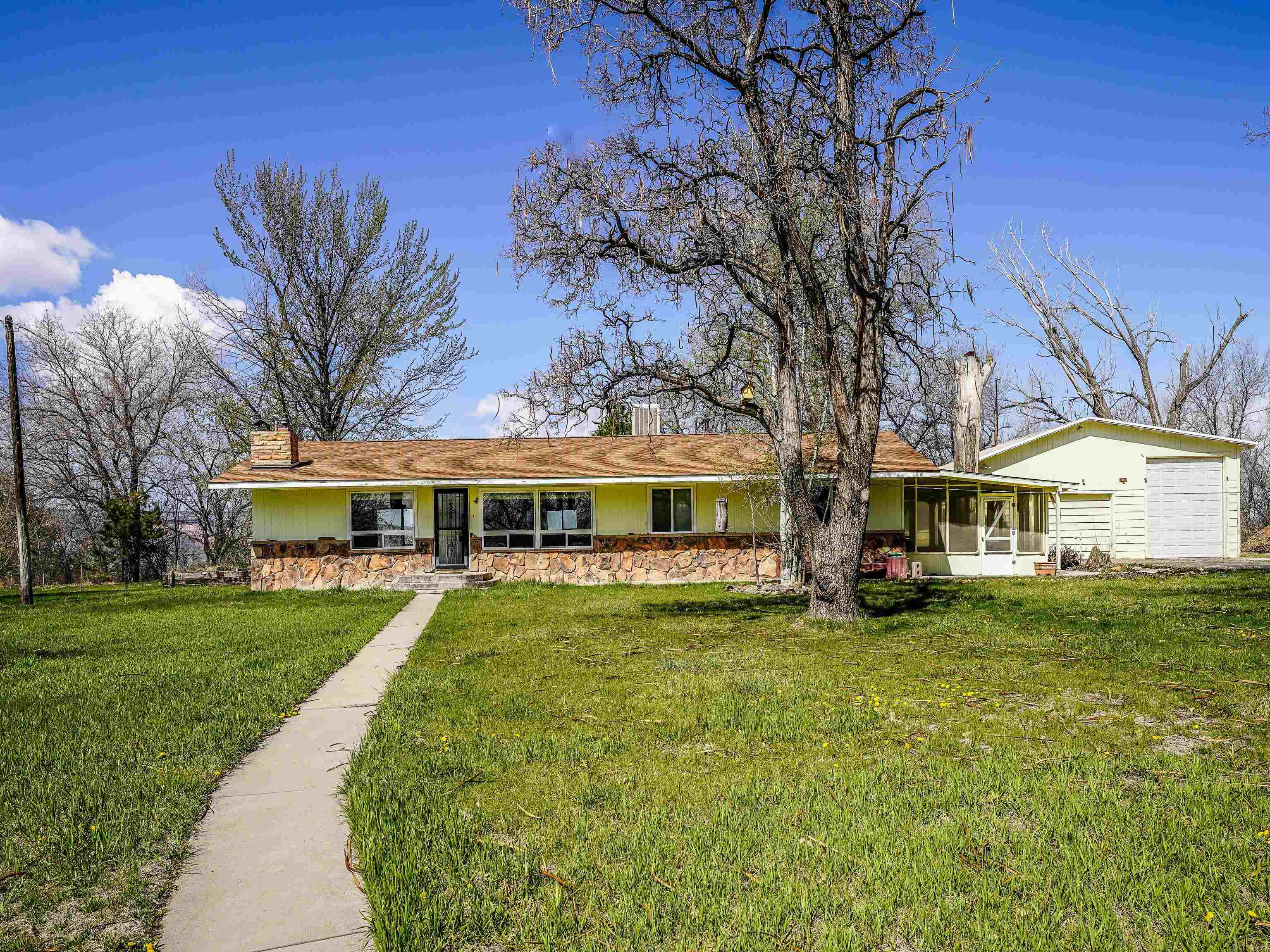 Welcome to your dream estate! Priced UNDER appraised value! This spacious 5 bedroom, 2 bath home with a full, finished walk-out basement or in-law suite is a rare gem. Located in north Grand Junction, close to conveniences and I-70 access. This home is situated on 12 irrigated acres, this property boasts 18 shares of water rights, a pond on property and elevated views of Colorado National Monument. Inside is carpeted but with beautiful oak flooring underneath. Cozy up to two fireplaces. The basement even has a kitchen and living area! A new roof was added in 2022 and new septic system in 2020. Enjoy the beautiful views from your large patio and fire pit. This property offers plenty of parking for your RV, toys, or other equipment, as well as barns, stalls and a heated 3-car garage/shop for storing your RV or projects. Don't miss out on the opportunity to make this beautiful property yours.