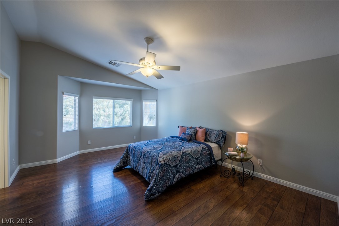 Oversized master bedroom offers a bay window with added space, laminate dark wood floors & a ceiling fan.