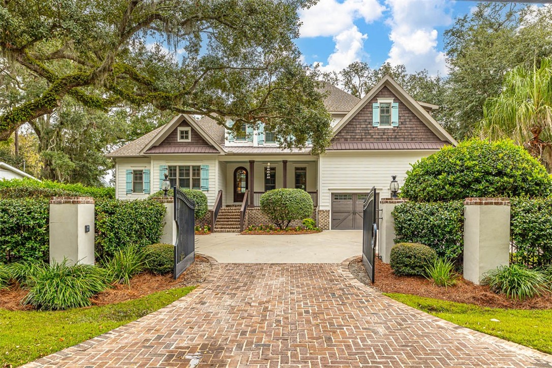 Stunning Southend home set on expansive double lots, less than two miles from the beach in St. Simons Heights. Greeted by a private, gated entrance, this Cape Cod-style haven exudes charm and elegance. The broad oak plank flooring introduces you to a sophisticated foyer, leading to a stylish formal dining room with a modern wine bar and cooler. The luminous great room, adorned with high beamed ceilings and one of two gas fireplaces, flows effortlessly into a spacious eat-in kitchen with an inviting keeping room and a second cozy fireplace. On the main level, find a serene primary suite with tranquil pool views, a meticulously designed bath with marble flooring, a generous soaking tub, a spacious walk-in shower, dual vanities, and his and her closets. A cozy guest suite complements the main floor, while the upper level showcases two additional bedrooms, two baths, and a multifunctional bonus room. Abundant storage space ensures every necessity has its place. Outside, the home boasts classic cedar shake and tabby finishes. Spend relaxing mornings on the covered front porch or host evening gatherings by the sparkling pool, enhanced by mesmerizing color-changing lights, a unique brick oyster fire pit, or on the covered back porch. The home also features a two-car garage, a beautifully curated landscape, and the peace of a fully fenced, gated property. Every detail of this home speaks to its unmatched allure.