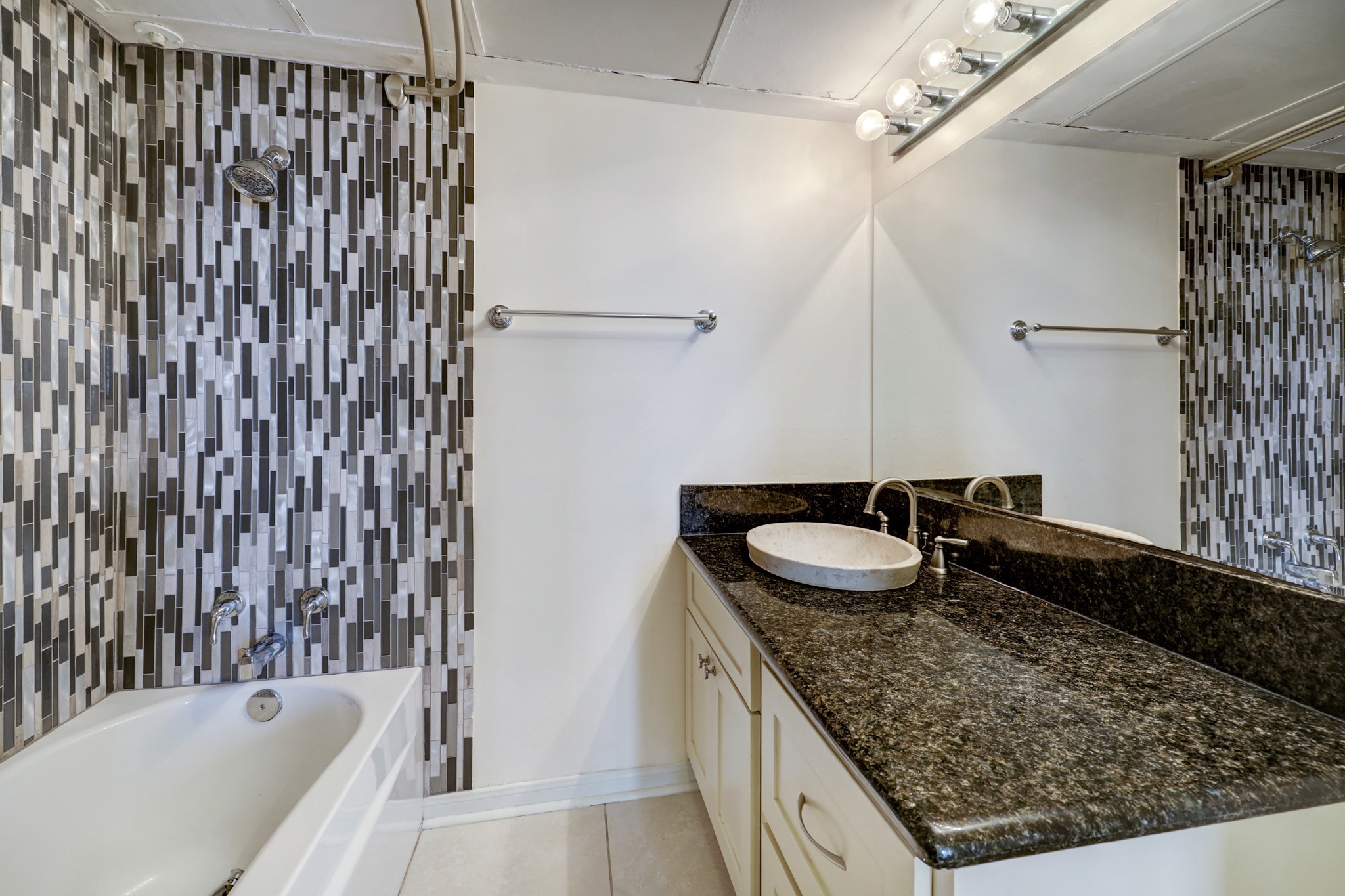 The secondary bath features a tub/shower, nice lighting, and a granite countertop sink area.