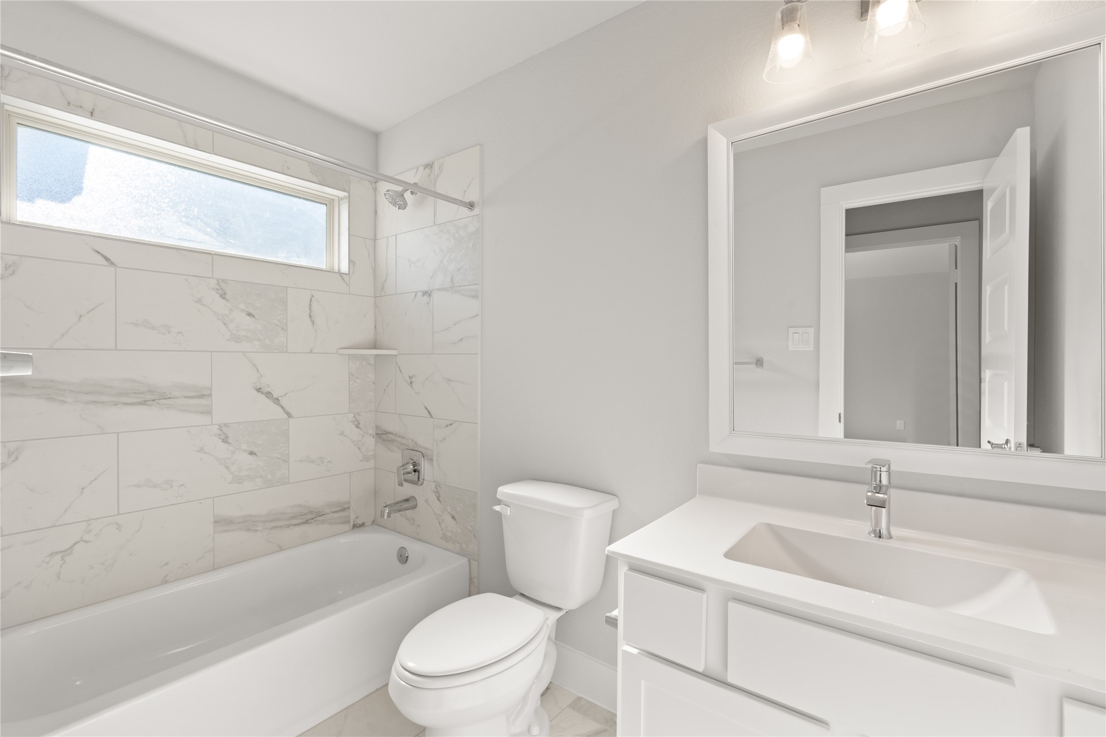 Secondary bath features tile flooring, bath/shower combo with tile surround, white stained wood cabinets, beautiful light countertops, mirror, dark, sleek fixtures and modern finishes.
