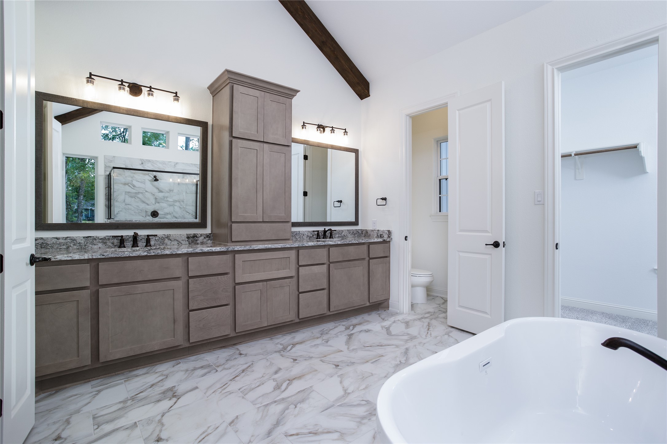 Another view of primary bath with double vanities and quartz countertops, raised ceiling, garden tub and walk-in closet.