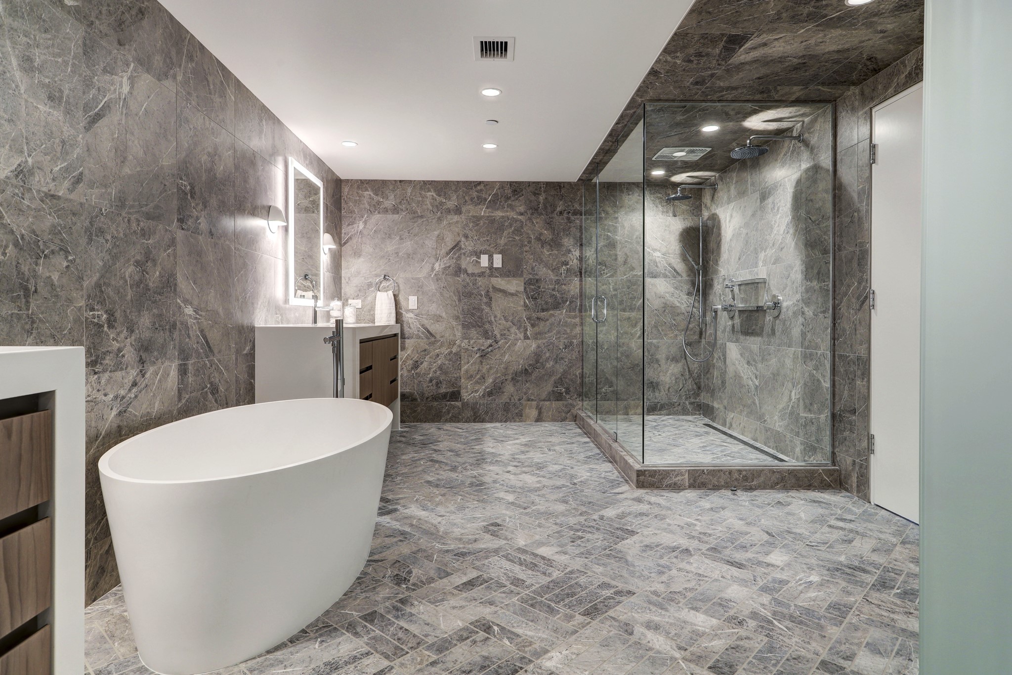 A shower, private water closet and floor-to-ceiling gray marble tile create an extraordinary spa experience in the main-floor primary en suite bathroom