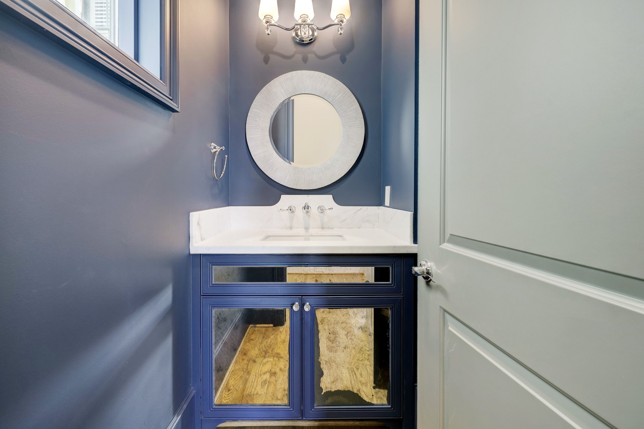 The formal powder bathroom features wood flooring, wall-mounted sconces, and a beautiful built-in vanity chest.