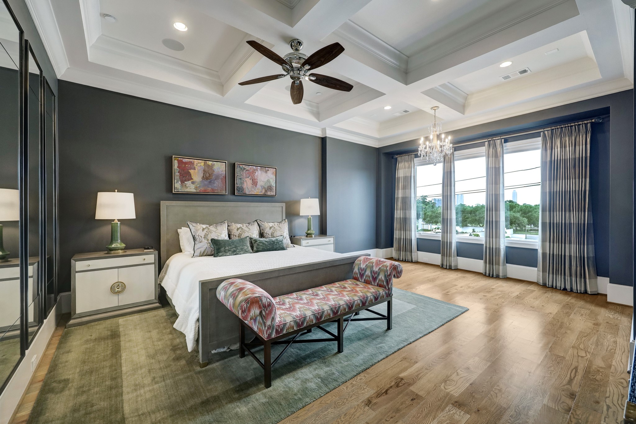 The large primary bedroom features a coffered ceiling, ceiling fan, crown molding, and large windows that bring in tons of natural light.