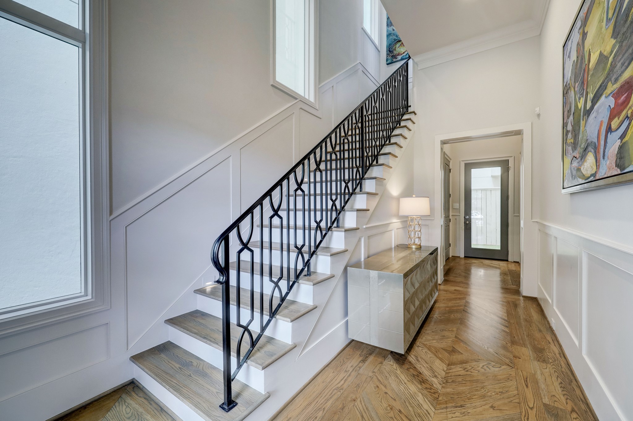 The inviting foyer features beautiful light wood flooring, wainscoted walls, access to the backyard, downstairs secondary bedroom, and stairs to the second level.