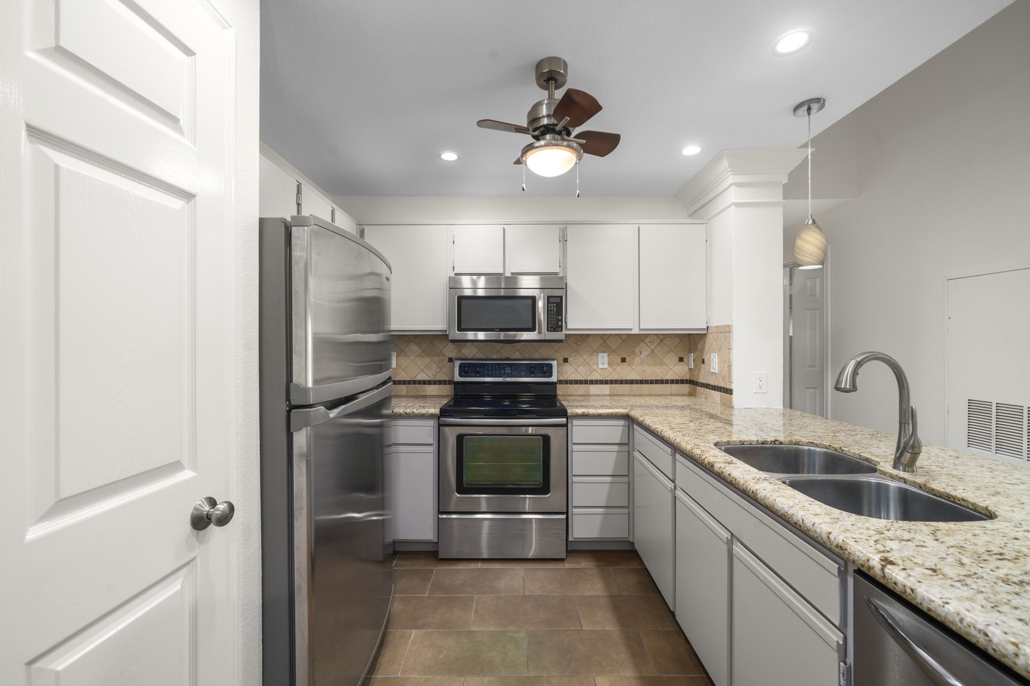 The stainless steel appliances perfectly complement the white cabinetry and warm beige marble, resulting in a harmonious and stunning visual blend.