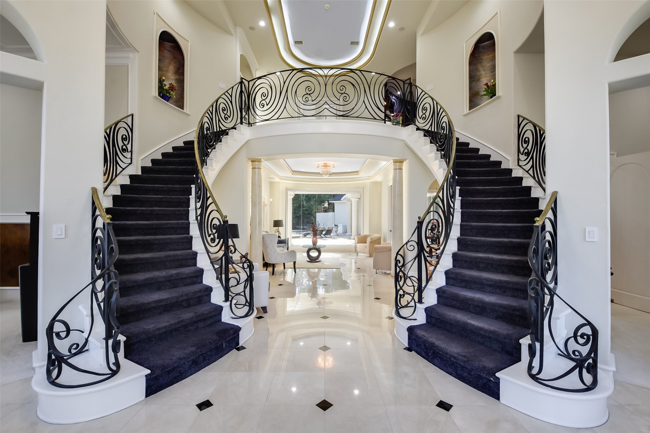 Inviting and impressive double staircase entry showcasing polished travertine floors and elegant chandelier.