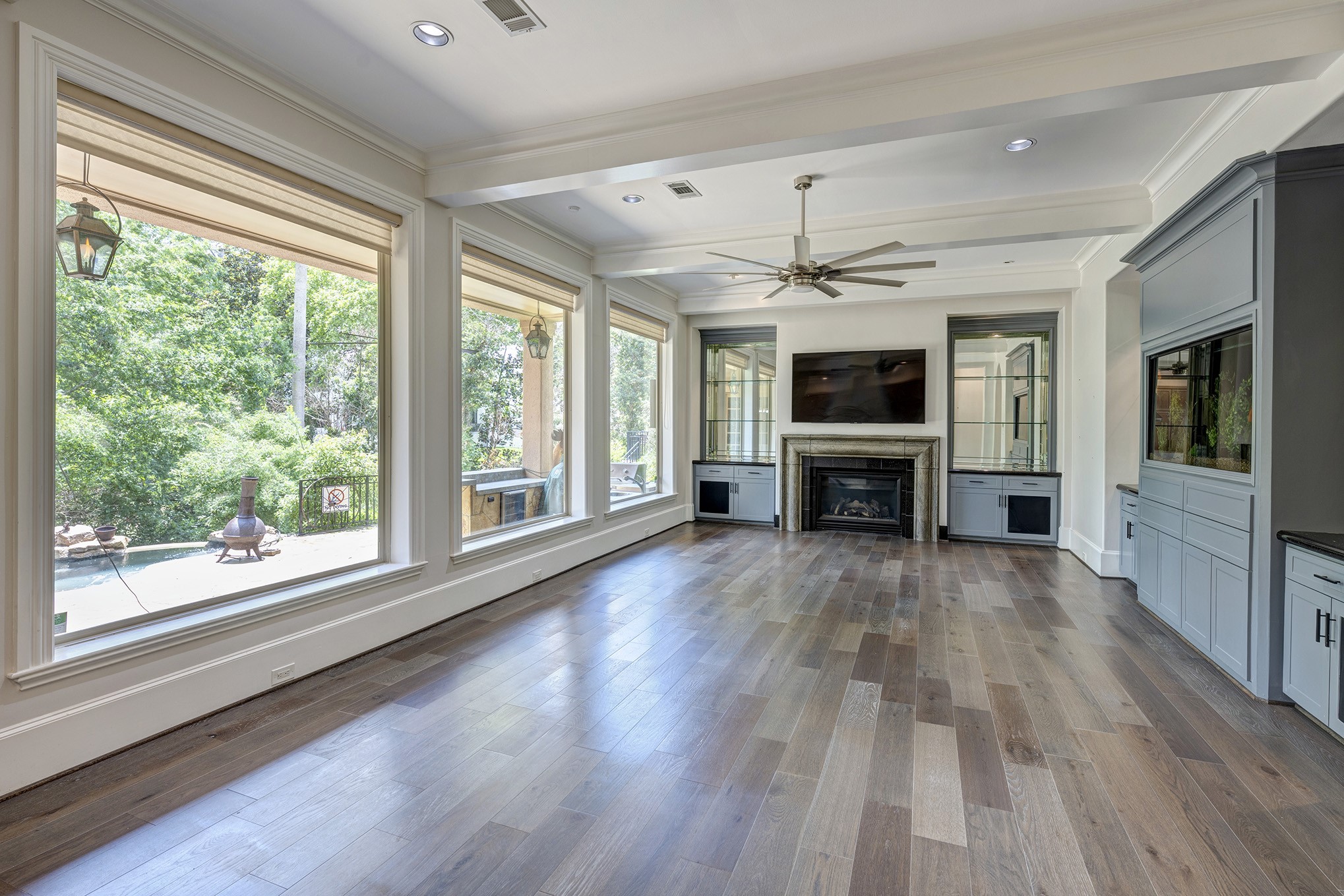 Living room with hardwood floors, fireplace, custom built-ins and wall of windows that look out to the picturesque backyard.