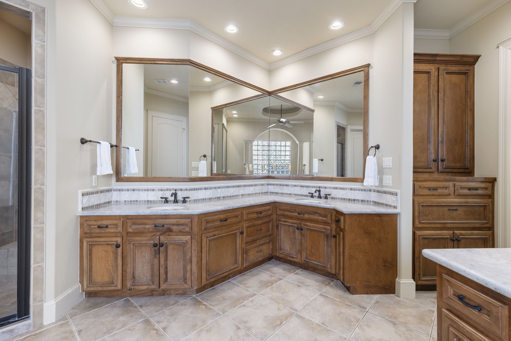 The spacious primary bathroom has high ceilings with recessed lighting, stone countertops accented with tile bordered backsplash and rubbed bronze hardware.