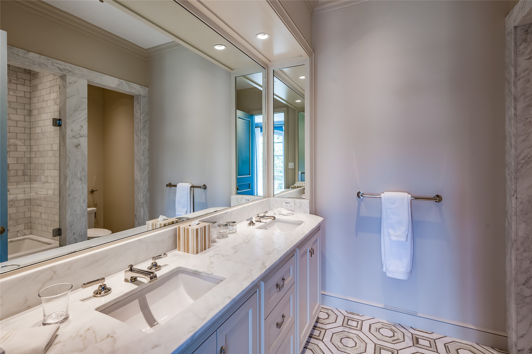 Guest bathroom includes dual vanity, hexagon tile and shower/tub combo with glass paneled door.