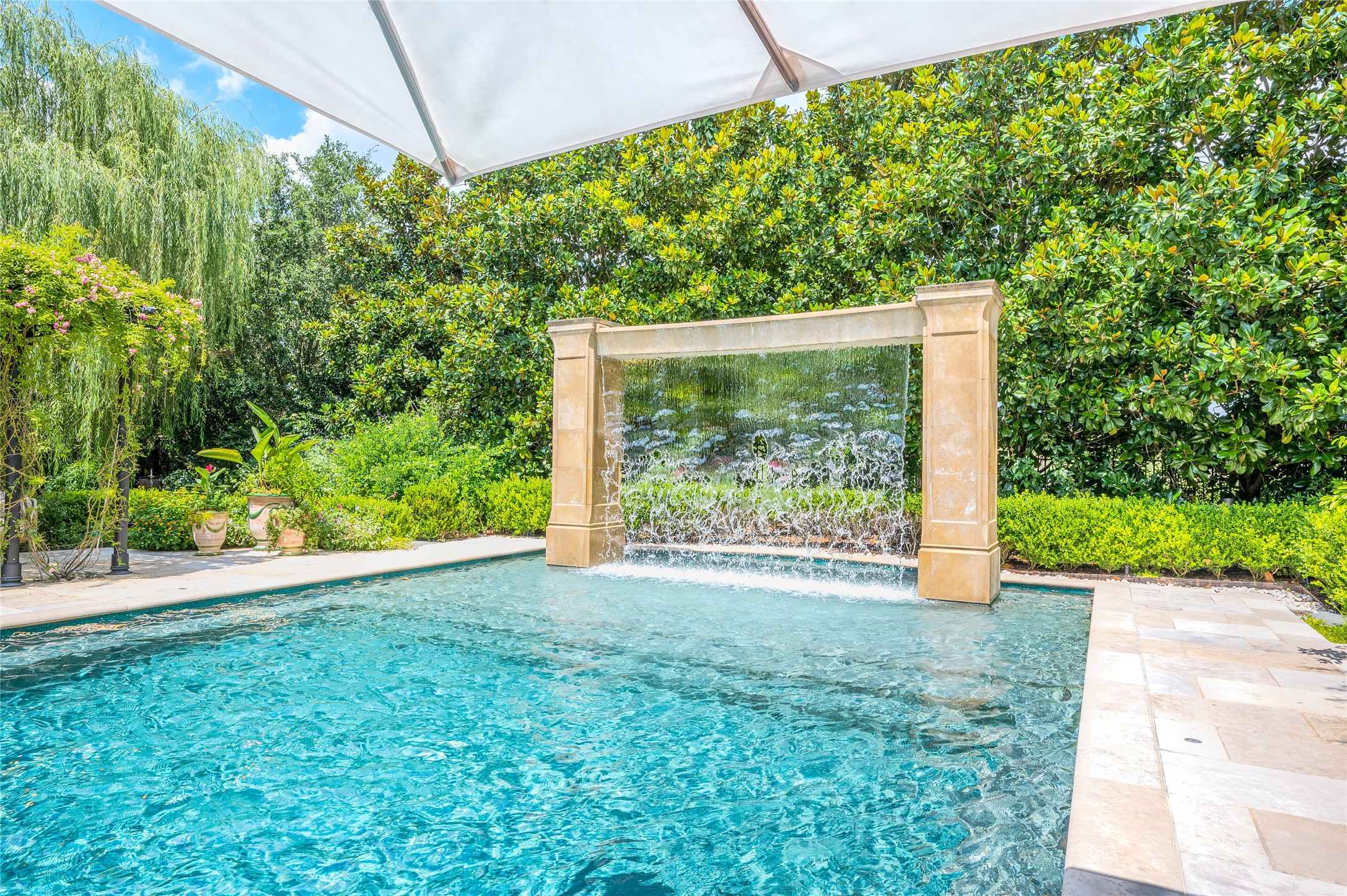 A calming water wall, along the lush canopy of towering trees, adds to the carefully curated ambiance within the pool and outdoor dining area.