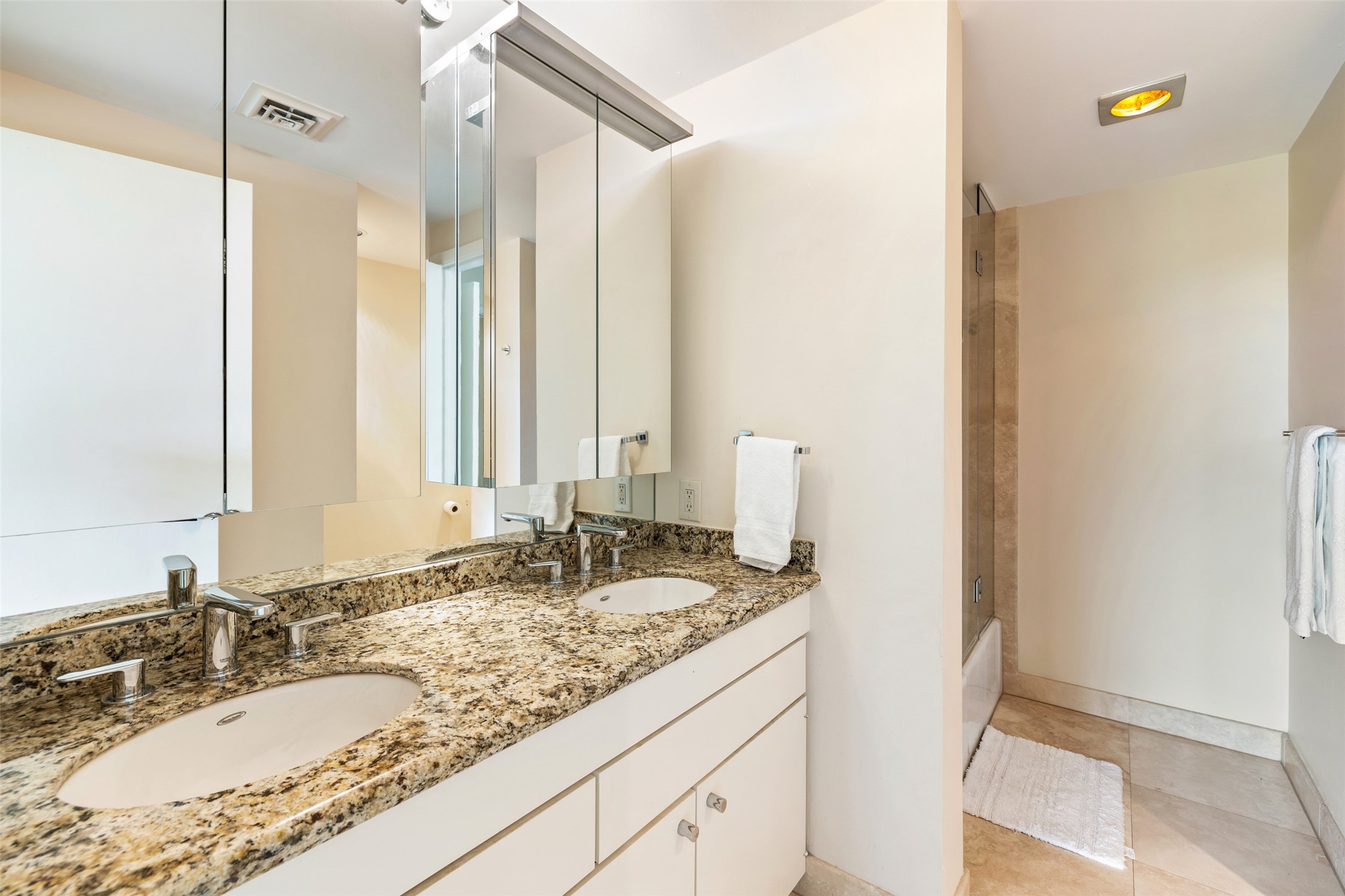 The primary bathroom has a double sink vanity equipped with granite countertops and mirrored backsplash and medicine cabinetry.