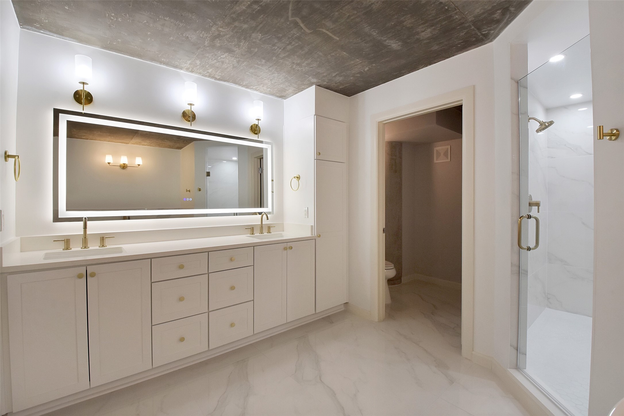 BEAUTIFULLY APPOINTED AND REMODELED ENSUITE PRIMARY BATHROOM FEATURES QUARTZ COUNTER, DUAL SINKS, CHIC LIGHTING AND AMPLE CABINETRY. NOTICE THE LARGE WALK-IN SHOWER TO THE RIGHT.