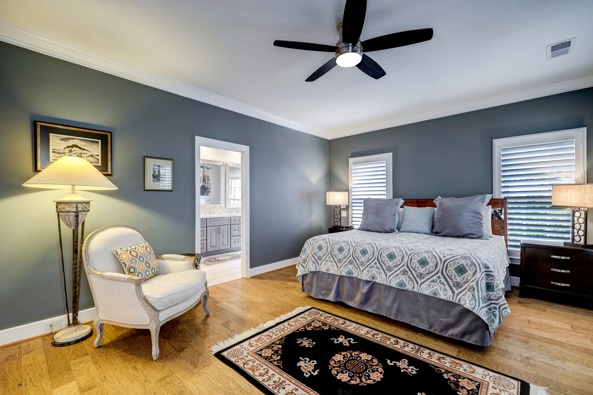 Large secondary bedroom with ceiling fan, hardwood floors and custom shutters. Through the doorway is the bath.