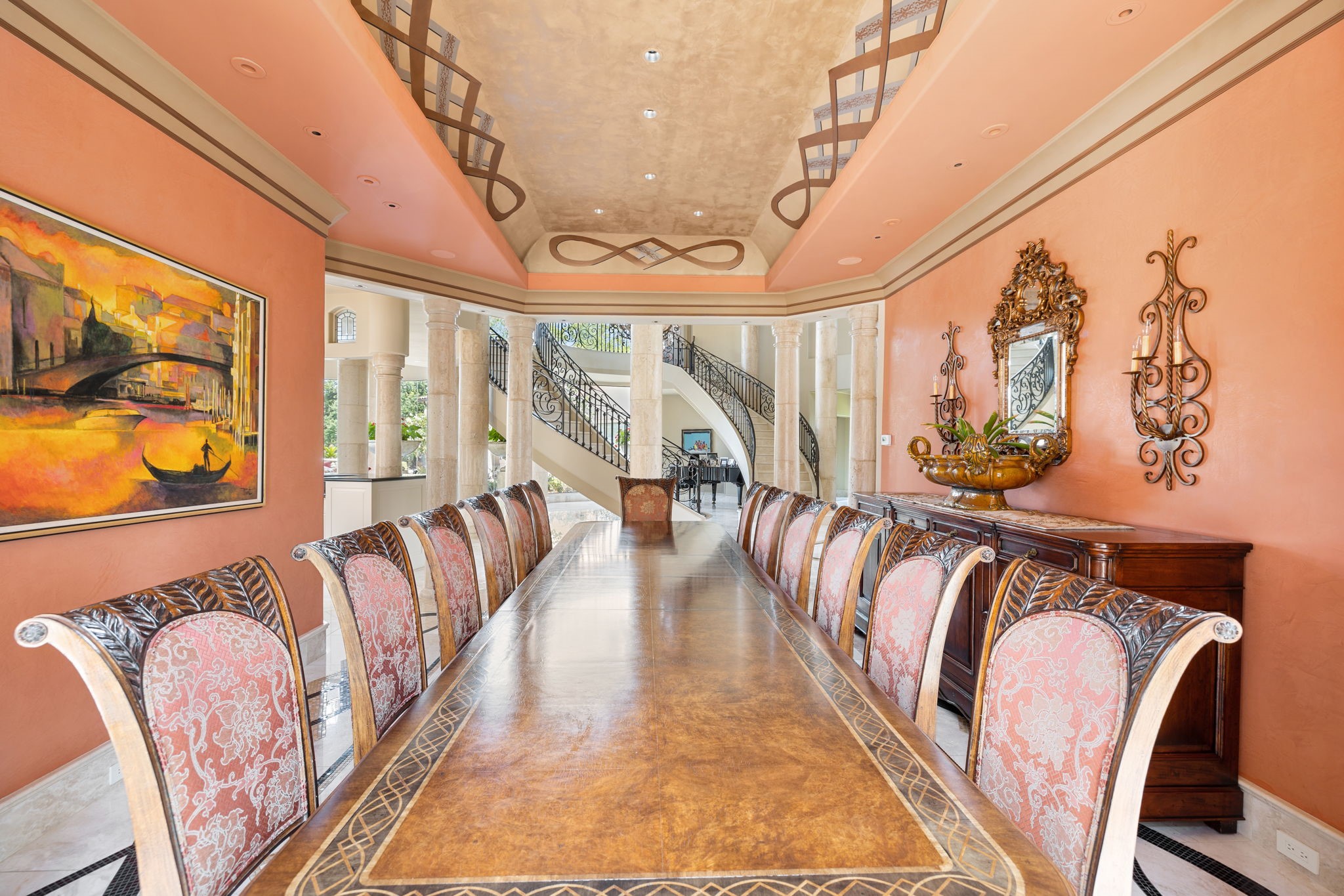 Just off a second axis of the Grand Entry is the Dining Salon, perfect for entertaining, as up to twenty guests are comfortably seated. The walls are swathed in terra cotta hued Venetian Plaster with Marble floors beneath your feet.  A rectangular cove ceiling is adorned with stencil accents. Off frame behind us is a view of the central Terrazza.