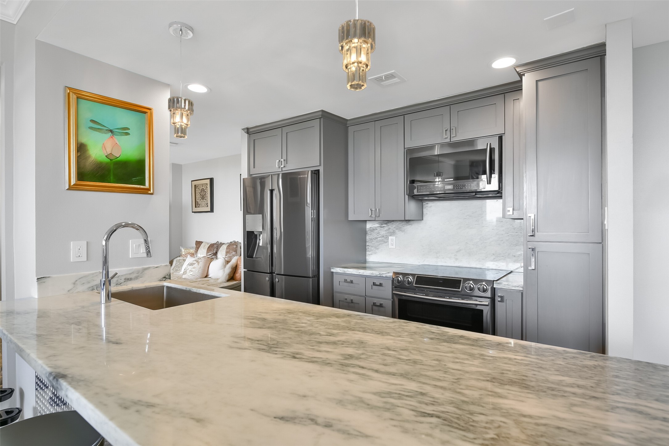 The kitchen features custom cabinets, marble waterfall island, stainless appliances and pendant lighting.
