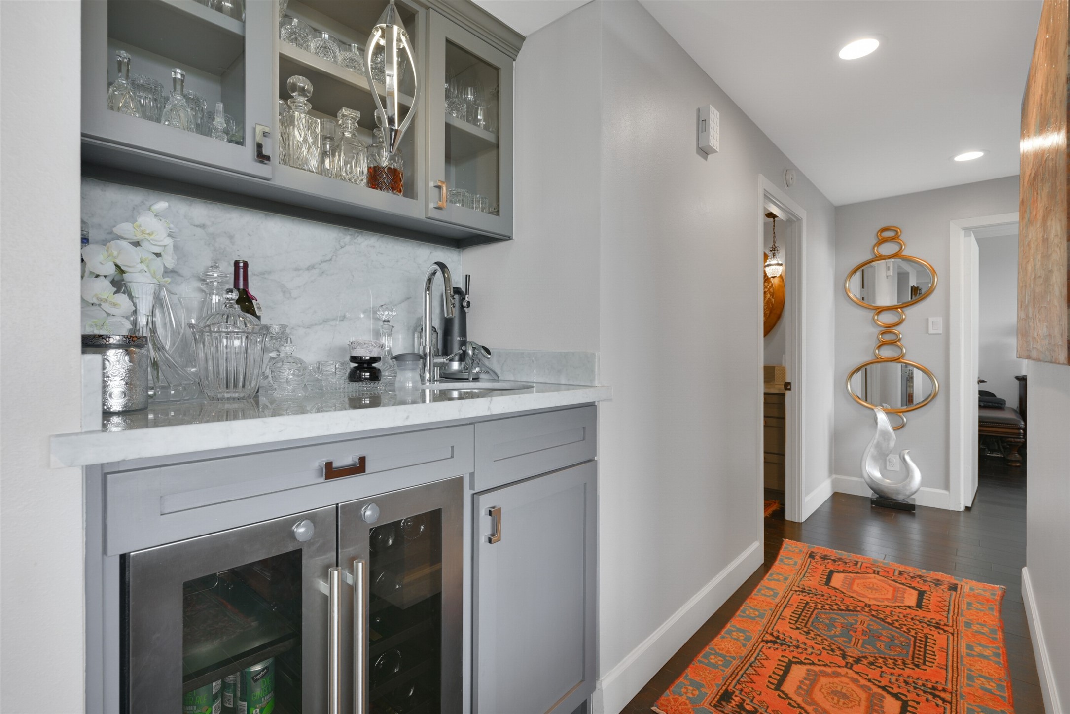 Elevate your entertaining with a chic wet bar with custom cabinets, marble countertop and backsplash, double wine fridge, glass front cabinets and an elegant pendant fixture.