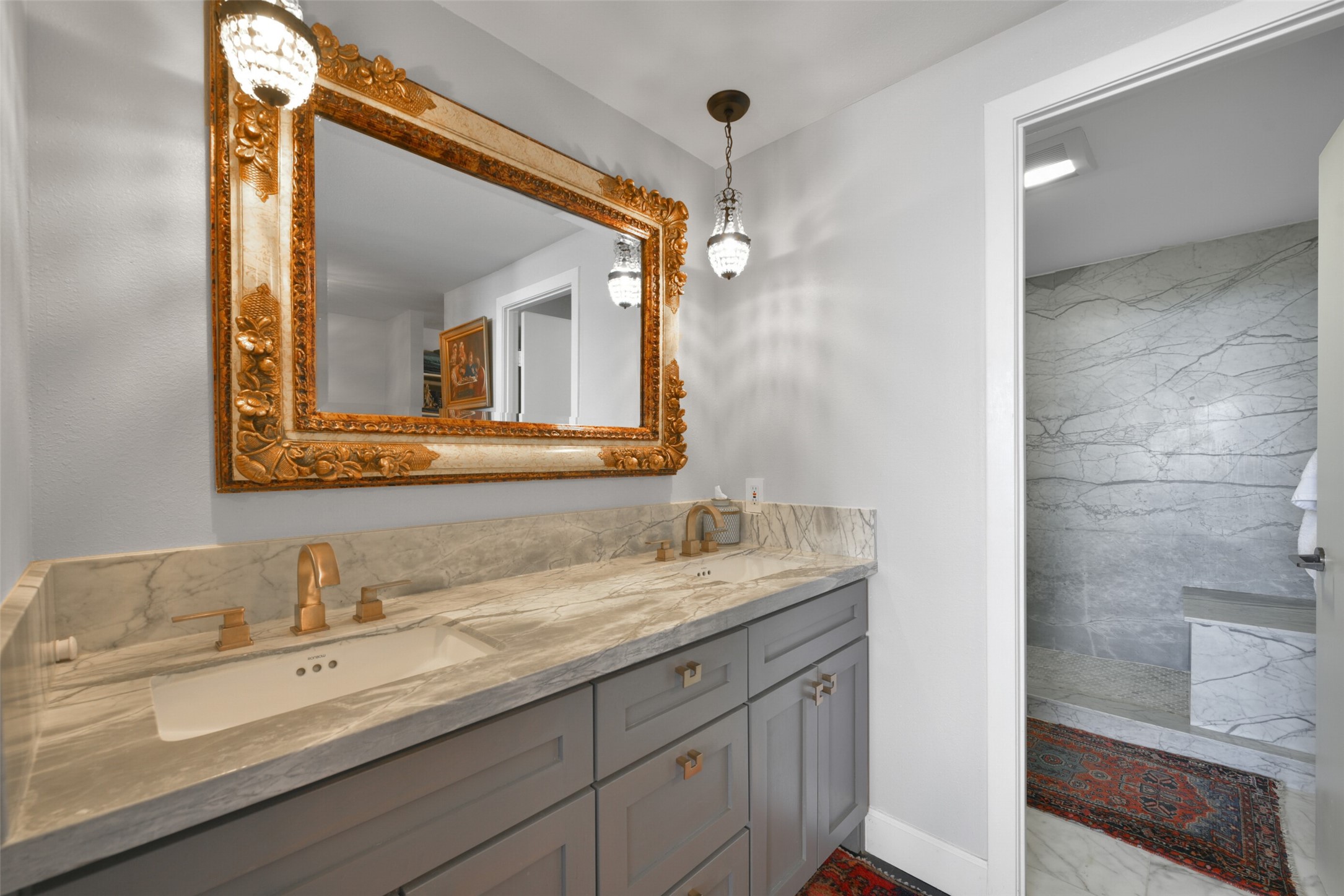 Indulge in luxury in the primary bathroom featuring a custom marble double vanity, framed mirror, brass fixtures/hardware and pendant lighting.