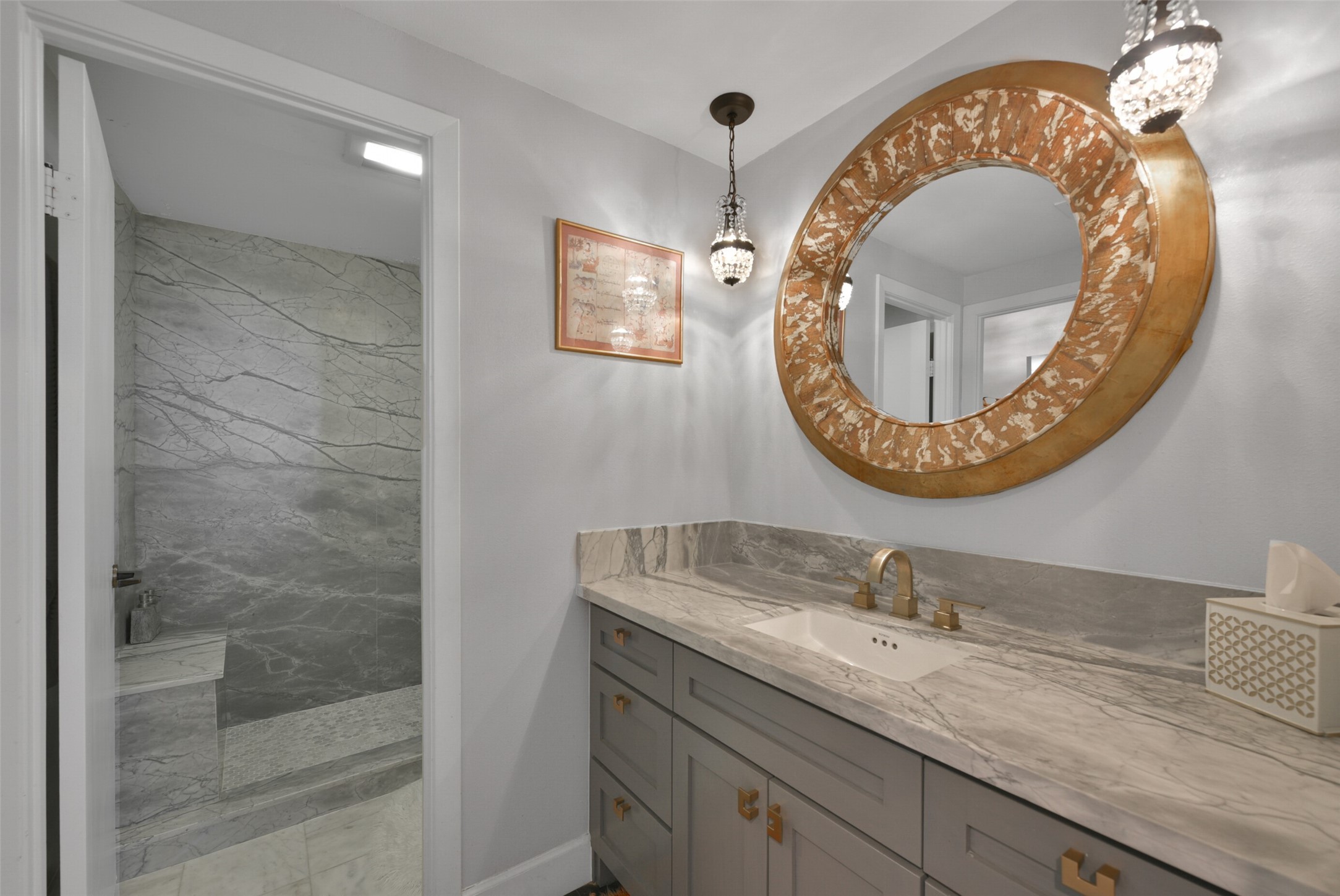 Luxurious secondary bath with custom marble vanity, brass fixtures/hardware, decorative mirror, pendant lighting and large marble shower with bench seat.