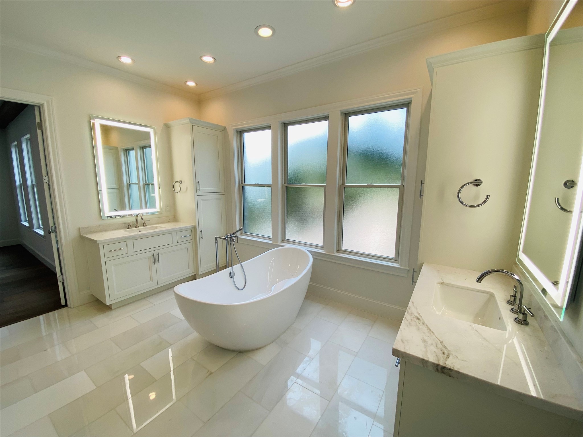 Luxurious primary bath with marble flooring & countertops, separate vanities, & free standing tub & separate shower