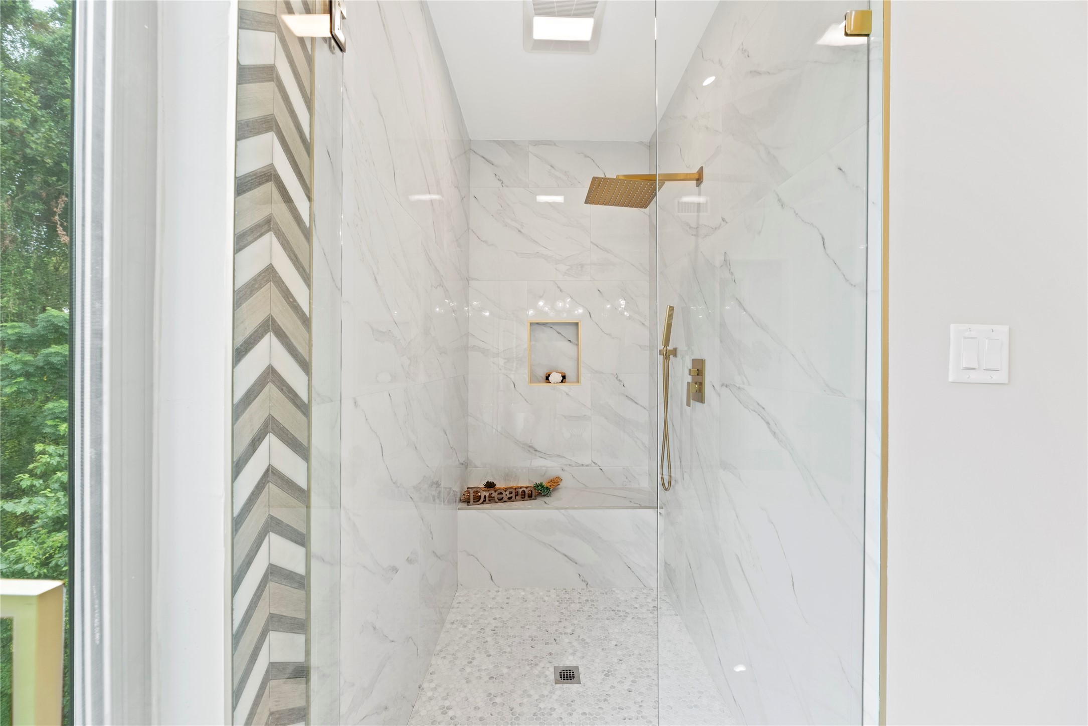 The separate [primary bath] shower features glass shower door, a rain water feature, brushed brass fixtures, & a bench!