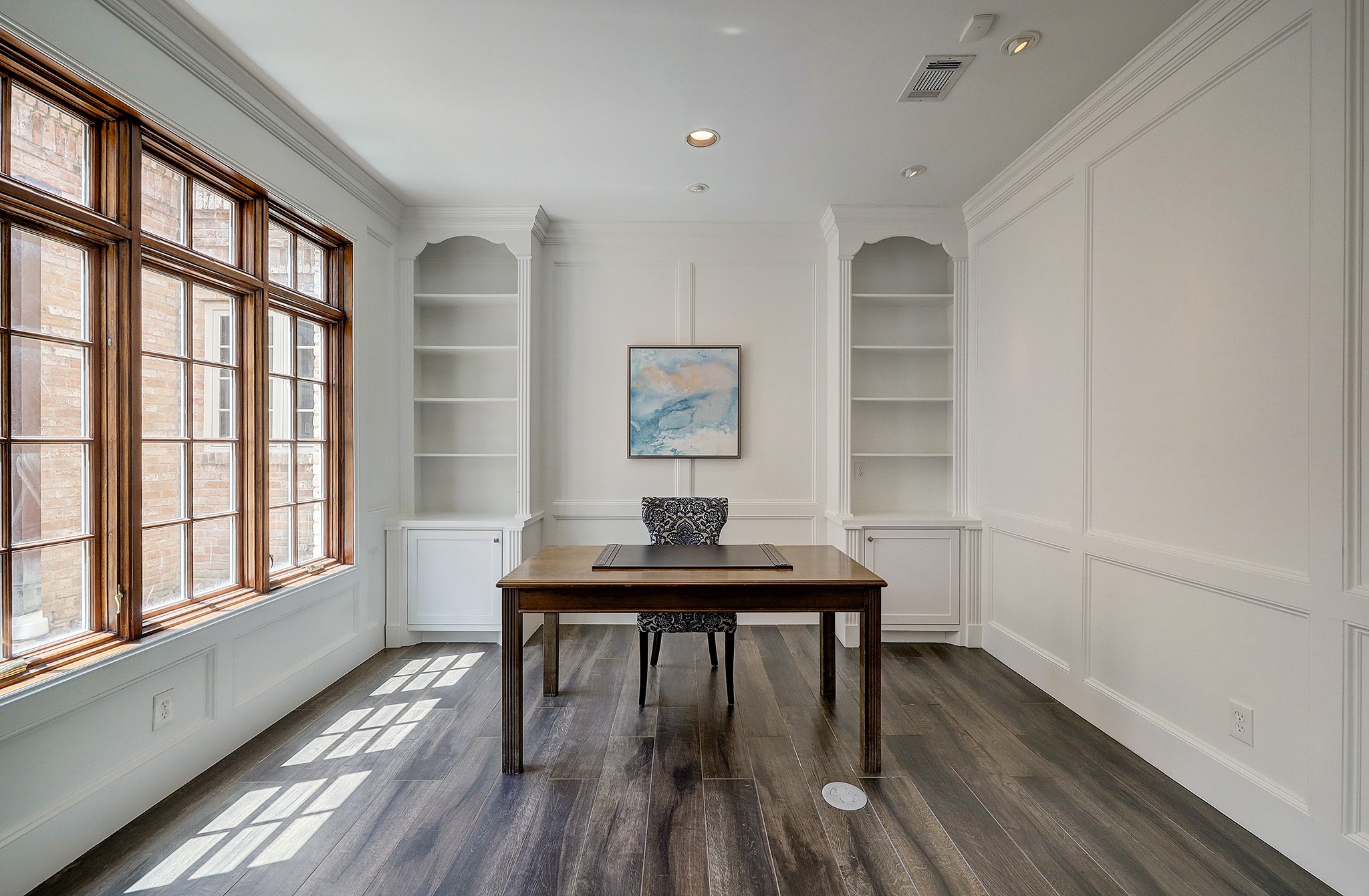 Study has custom built-ins, wall panel moulding and a wall of large windows.