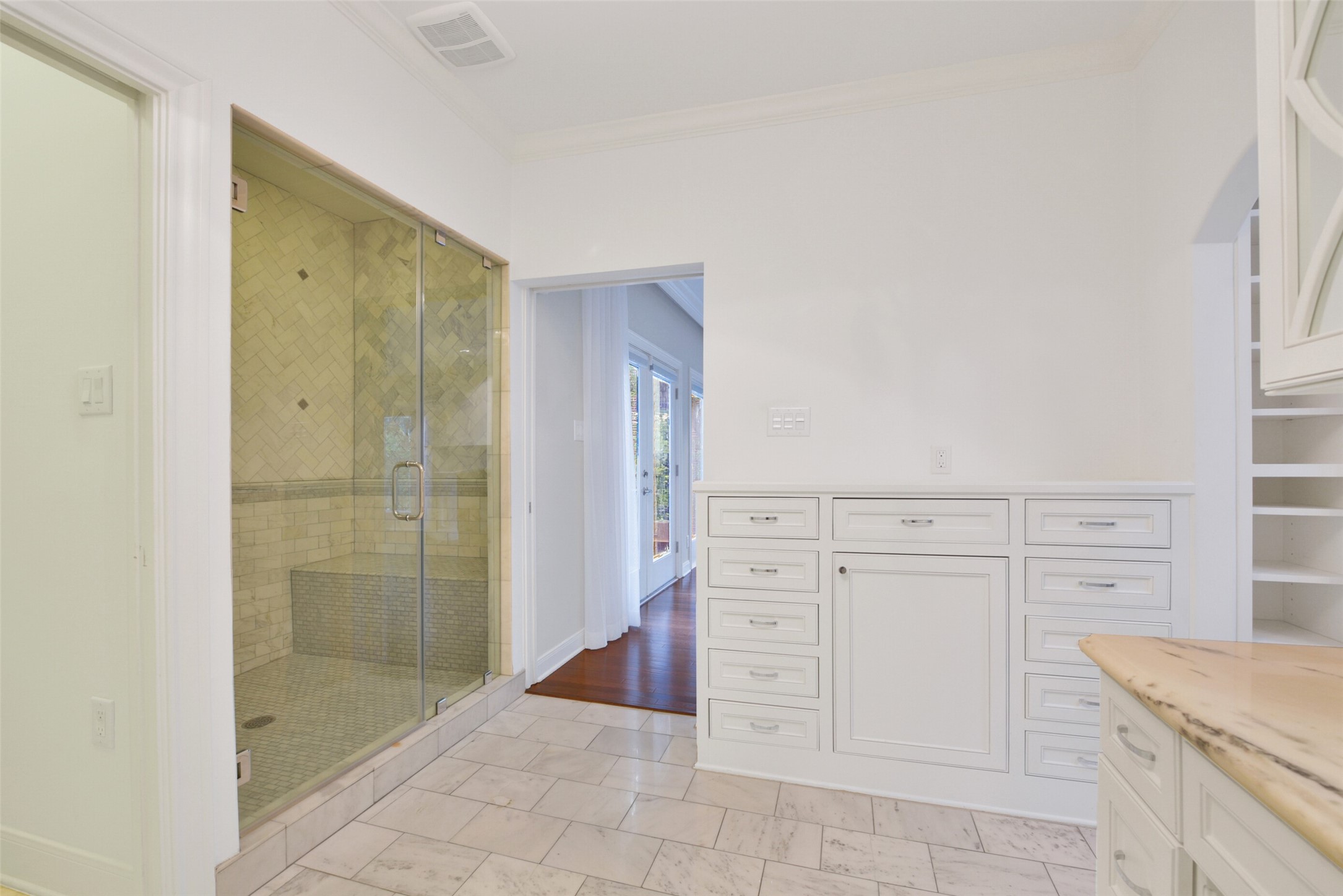 Another view of the first of two primary baths featuring built-in dresser, seamless glass shower enclosure. Each bath offers a private walk-in wardrobe with custom cabinets and built-ins.