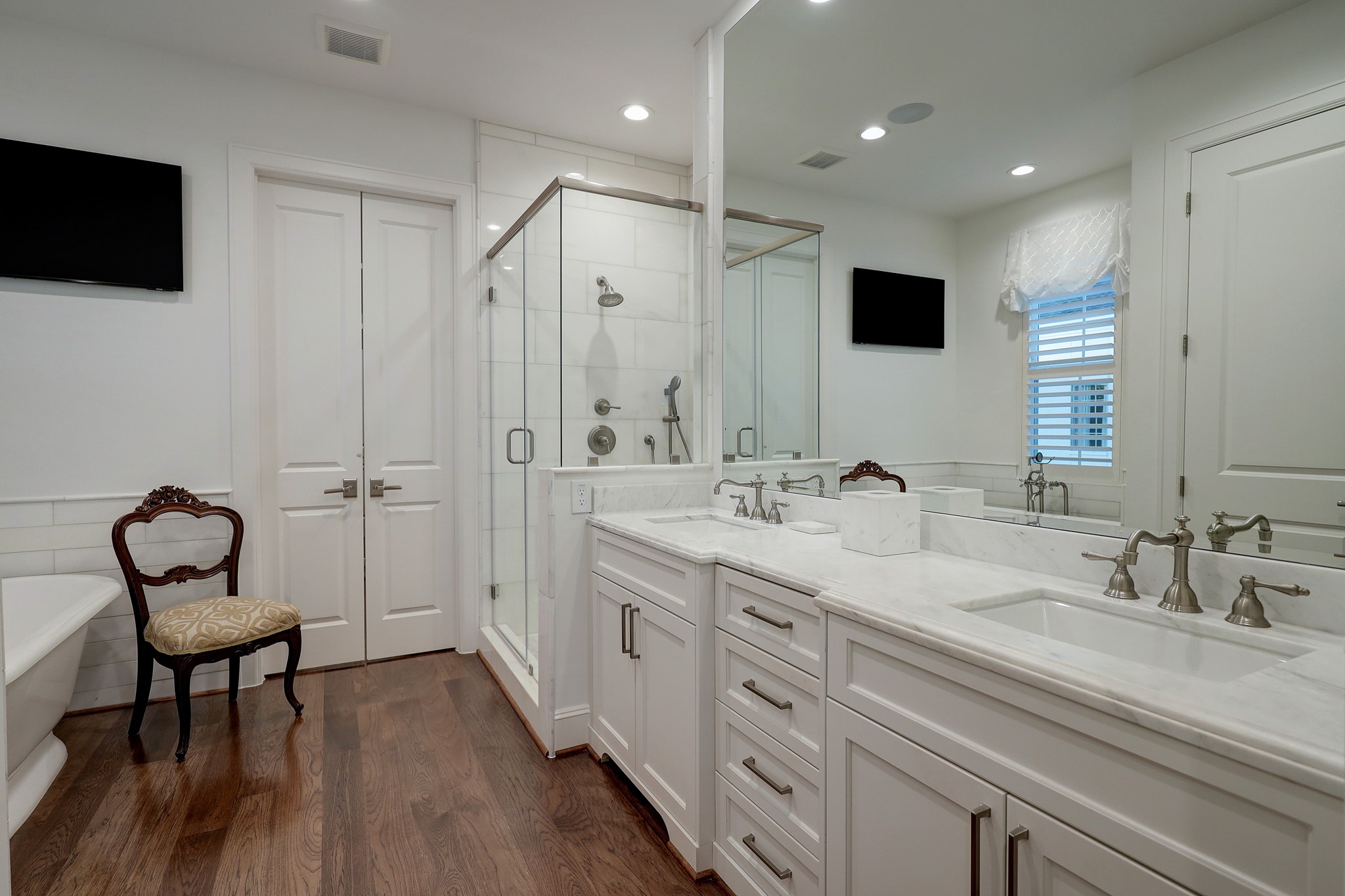 An oasis of its own, the primary bath features marble counters with dual sinks, an Albert & Victoria free standing soaking tub with marble surround and plantation shutters, and a dual-head walk-in shower with marble surround, floor, and seat.