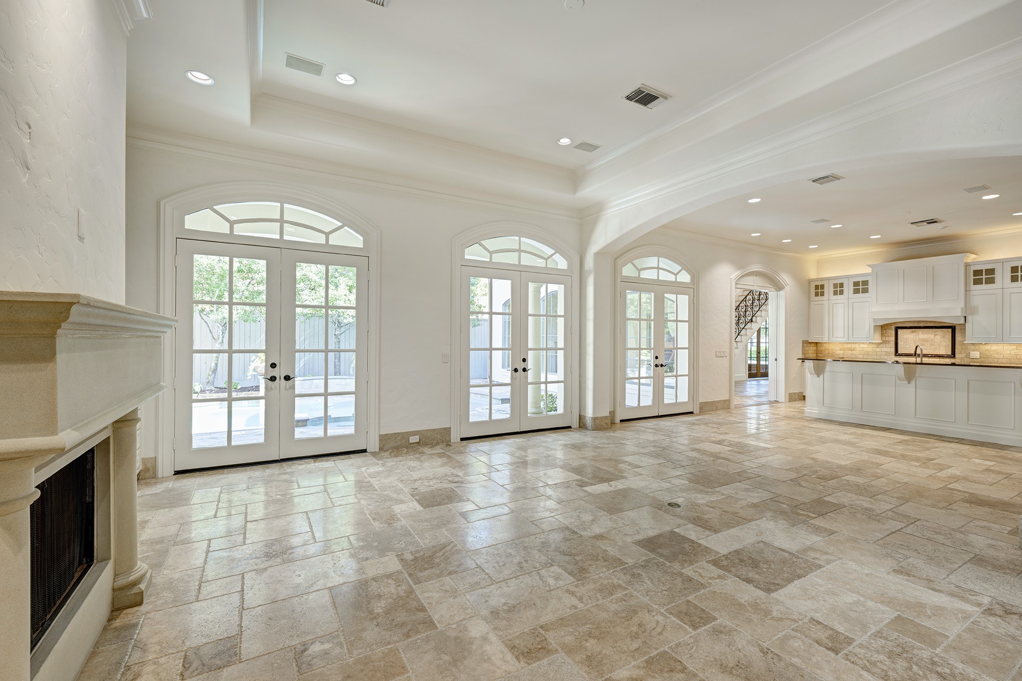 Open concept family room and kitchen with stone floors and wall of french doors that lead to the the backyard oasis.
