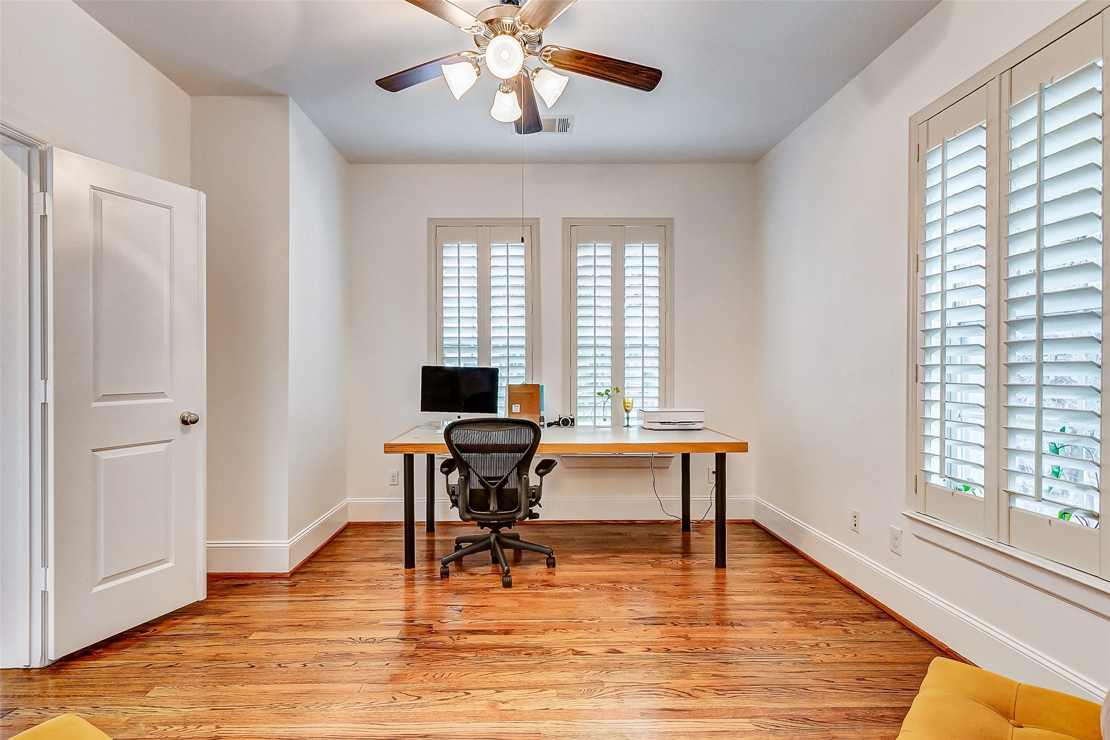 Spacious first floor bedroom boasting gorgeous wood flooring, soaring ceilings, and custom plantation shutters.
