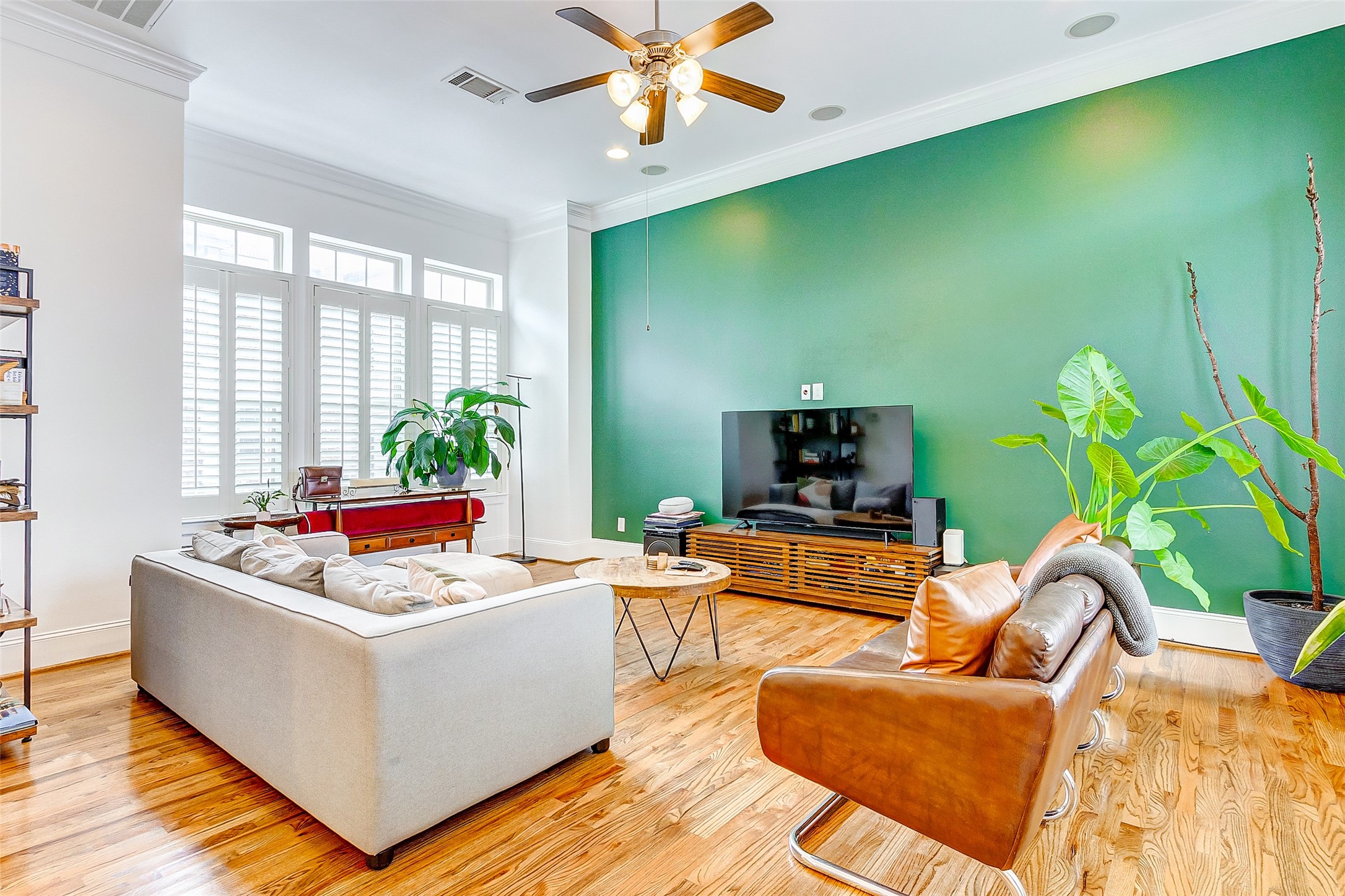 Welcome to you spacious family room featuring soaring ceilings, stunning emerald accent wall, gorgeous wood flooring, plentiful natural lighting, custom plantation shutters, and comes complete with built-in speakers!