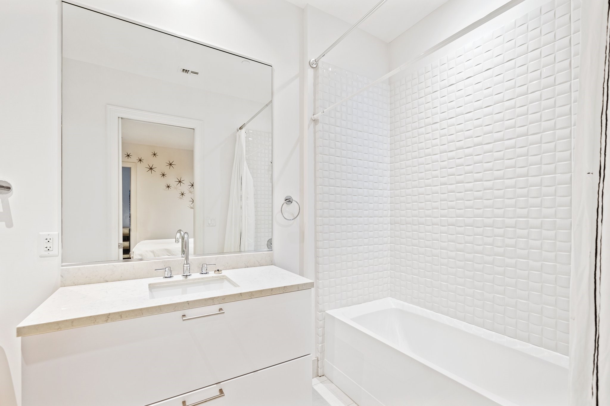 The 3rd bedroom's ensuite bathroom showcases modern elegance with a large mirror and a stone-topped vanity. The cube-tiled shower and bathtub combination offers both function and relaxation in a pristine setting.