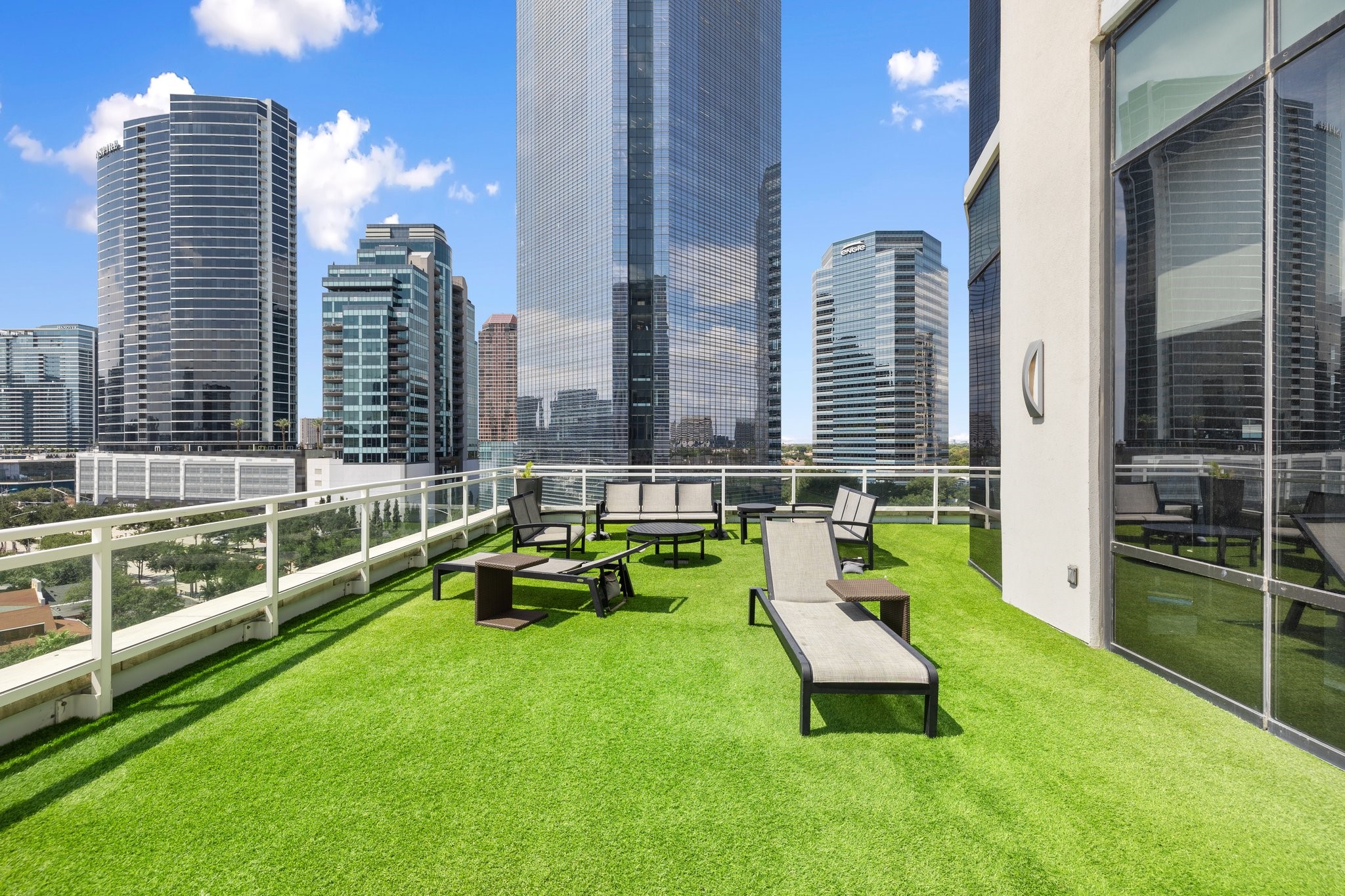 This rooftop deck, surrounded by skyscrapers, offers a serene urban escape. The vibrant green turf contrasts with the city backdrop, providing a perfect spot for sunbathing or gatherings. Modern lounge chairs and an unobstructed view make it a versatile haven amidst the city's hustle.