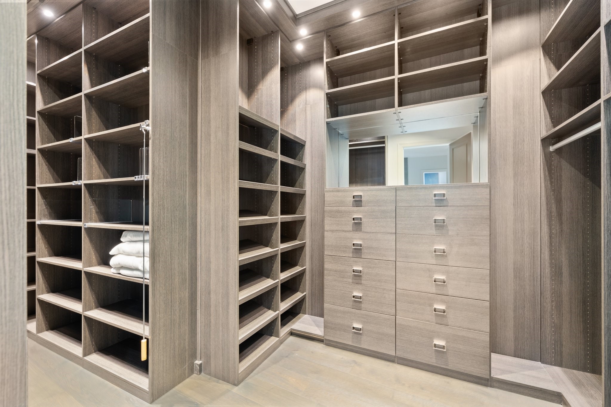 Sophisticated custom California closet in the primary bedroom, showcasing elegant wood finishes, multi-tiered shelving, and ample drawer space for optimal organization.