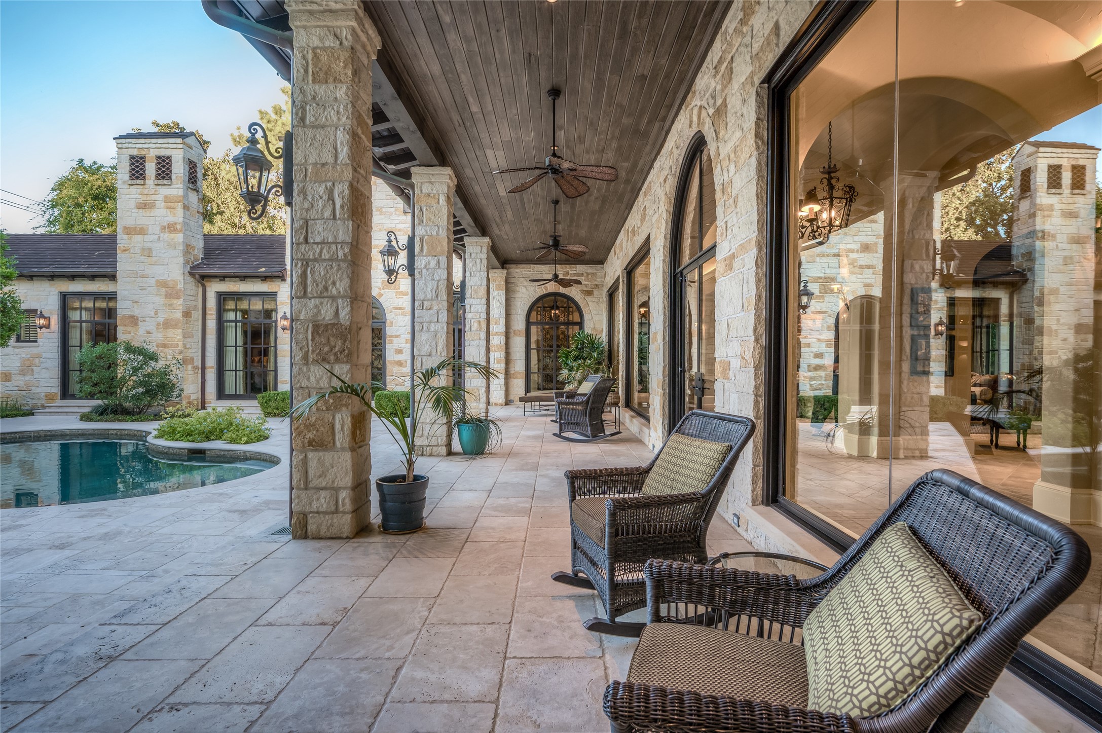 [Outdoor Living / Dining Area]
This view reveals the inviting outdoor living and dining room with raised stone fireplace. Paneled door at rear opens to the full pool bath and changing room. Note butted glass window in rotunda bar.